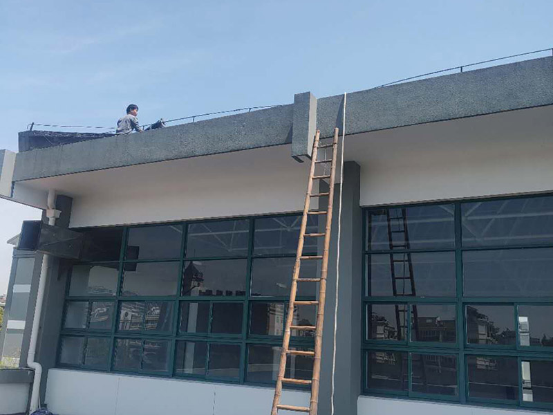 學校屋頂防水：屋頂做防水前，要先對需要防水施工的屋頂基層進行清潔，因為很多防水施工中要避免一些雜物、塵土等，打掃干凈了更有利于防水施工效果。屋頂防水施工就與室內防水施工差不多，室內的地漏、水管位置等都要重點涂刷，而屋頂中的水落口、女兒墻、檐口、陰陽角等位置也要先進行針對性的施工，也被稱為附加層施工。屋頂施工防水需要不少材料，特別是防水用的改性瀝青卷材、防水涂料等等，先對基層鋪貼一層防水卷材，其厚度要符合要求，尺寸根據屋頂面積進行裁剪。卷材一般歐式用熱熔的方式來鋪貼，也就是需要借助火焰噴槍來加熱進行滾鋪、粘貼，卷材從檐口處與屋脊平行的方向由下而上進行鋪貼。卷材的各個搭接處都要用噴槍來加熱粘結牢固，并且在邊緣末端收頭處要用密封膏來嵌填嚴密好才行。卷材鋪貼好后，要再一次進行屋頂清潔，保障干凈、干燥的施工環境，這時候就可以進行第一層的防水涂料刷涂了，第一遍一定要涂滿，不能出現遺漏、裂紋、氣泡、黏合不牢固等現象。